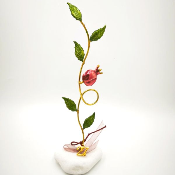 A handcrafted tabletop good-luck charm for 2027 featuring a pomegranate branch and leaves set upon a pebble